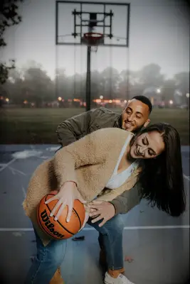 Couple plays basketball while posing for the camera. 