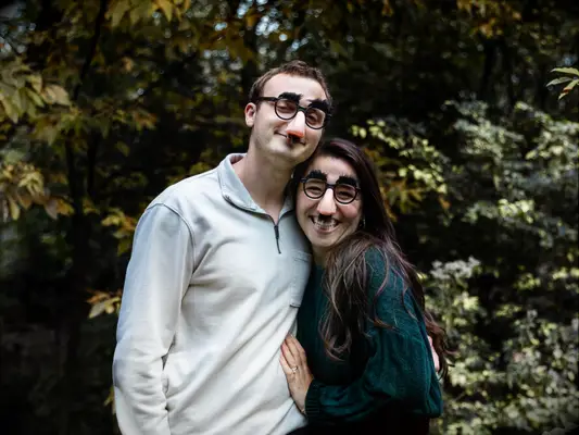 Couple poses for the camera wearing novelty disguises. 