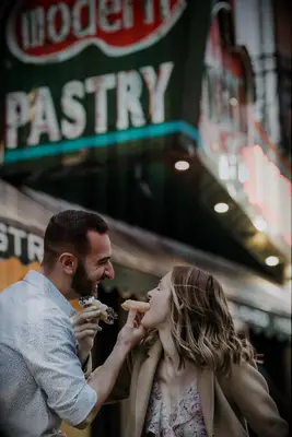 Couple feeds each other cannolis outside their favorite pastry shop. 