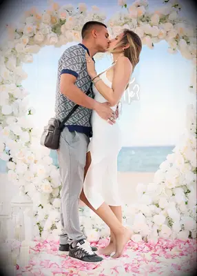 Couple kissing on a beach in front of a heart made of white roses
