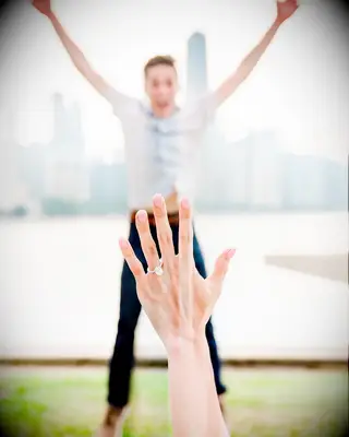 Engagement ring selfie in front of partner jumping in the air
