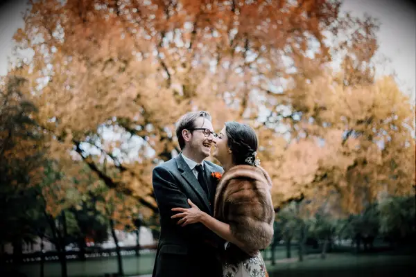 A woman and a man laugh together in front of an autumnal tree for their engagement photo