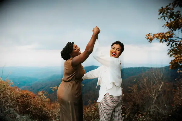 Two women laugh together with mountains in the background for their engagement photo