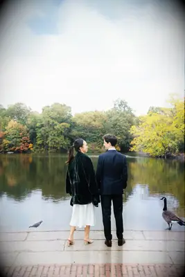 A couple stand at a pond together with some Canada geese