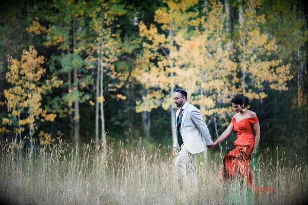 A groom and bride walk together through a meadow for their engagement photoshoot