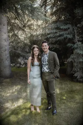 The couple smile for the camera outdoors among the trees