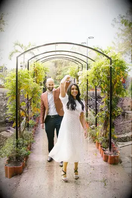 A man and woman twirl under a greenery-laden archway for their engagement photo session