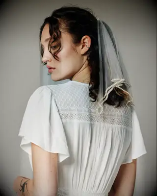 Model wears a chic short veil with pearls stitched on the hem. 