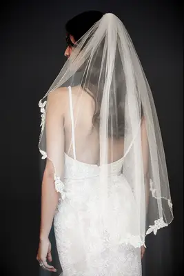 Model wears an elbow-length veil with floral trim. 