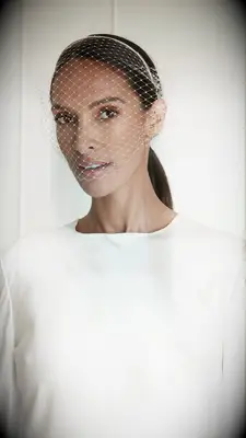 Model wears a headband with a birdcage veil attached. 