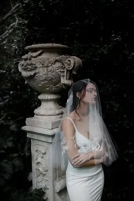 Model stands in a garden and wears a sheer veil over her face. 