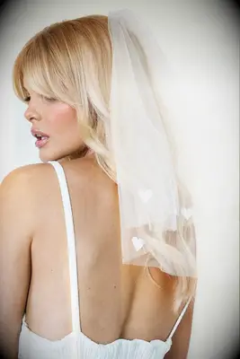 Model wears a short veil with hearts stitched at the hem. 