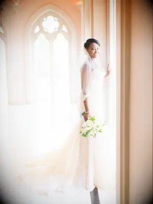 bride wearing lace fit-and-flare dress with train stands in chapel corridor