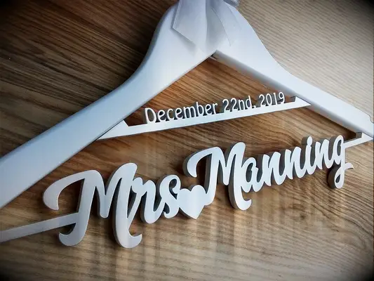 Thick white wooden hanger with future last name and wedding date on base