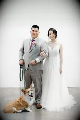 A happy couple smiling at the camera with their corgi