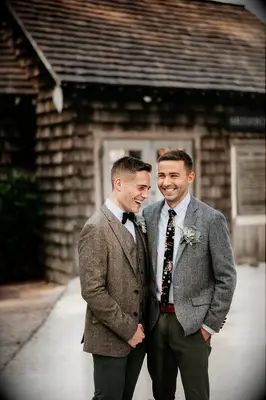 Two grooms smile at the camera in grey and brown suits