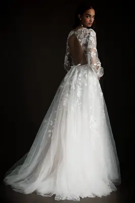 Model wears a floral long-sleeved wedding dress with a bow at the back. 