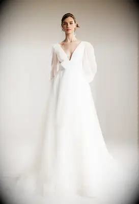 Model wears a long-sleeved wedding dress with a bow at the waist. 