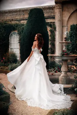 Bride wears an off-the-shoulder wedding dress with a bow in the back. 