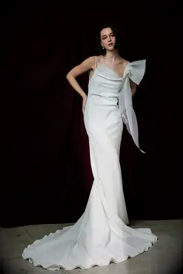 Model wears a white mermaid-style gown with a large bow on the strap. 