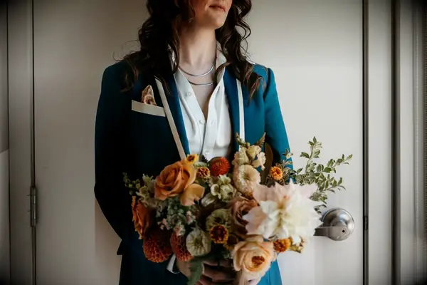 Woman wearing blue lesbian wedding suit from duchess clothier holding bouquet of flowers