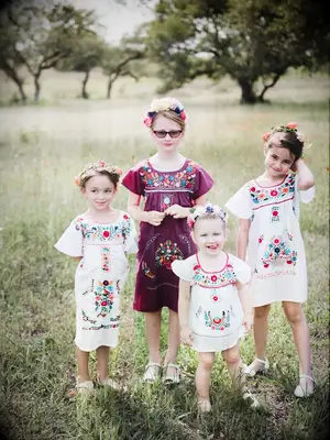 Four flower girls wearing colorful traditional embroidered Mexican dresses.