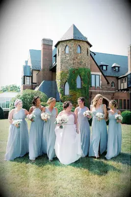 A bride walks with her wedding party over the lawn of their wedding venue.