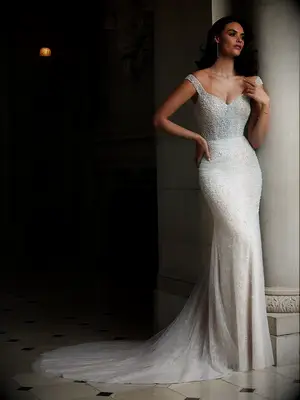 model stands against stone column wearing beaded fit and flare wedding dress