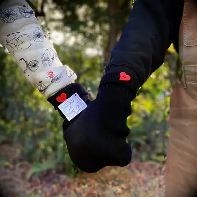 Couple holding hands wearing matching black mittens with red heart button