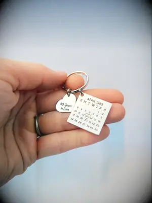 Silver keychain that features a calender highlighting an anniversary date. 