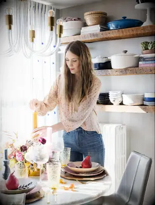 An interior designer arranges dining items on a table. 