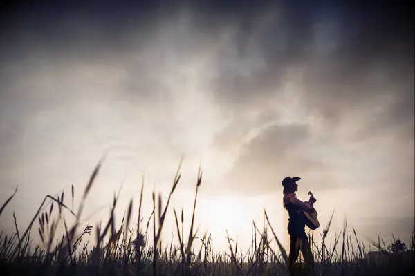Semi-silhouette of a Cowgirl with a guitar in the landscape during the sunrise