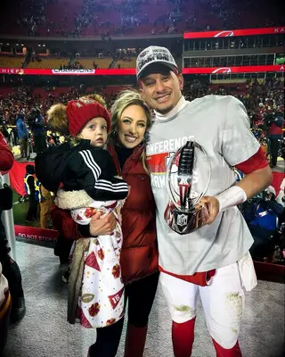 Brittany and Patrick Holmes smile with their child while celebrating a big win on the football field. 