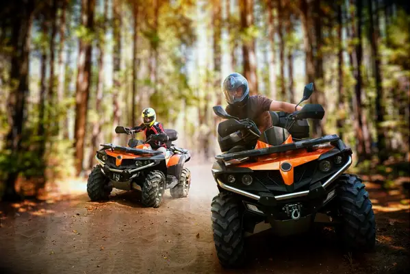 Two friends race through a forest on ATVs. 