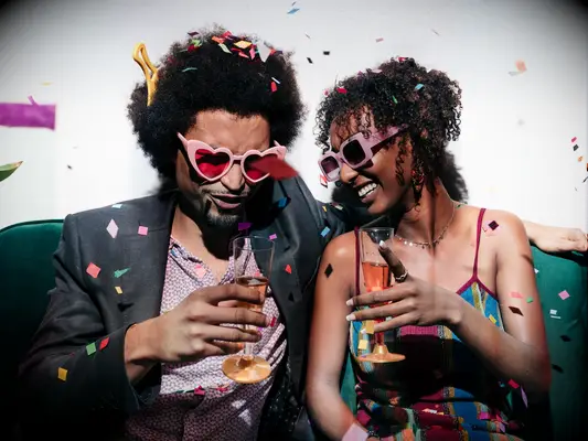 Couple covered in confetti wearing sunglasses with champagne flutes