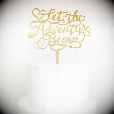Gold cake topper reading Let the Adventure Begin