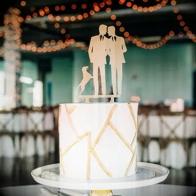 White and gold cake with cake topper of same-sex couple and dog