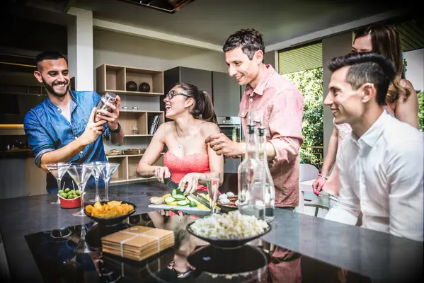 Group of friends mix cocktails and laugh at a house party. 