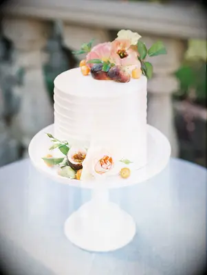Simple one-tier wedding cake with fresh fruit and flowers atop white cake stand