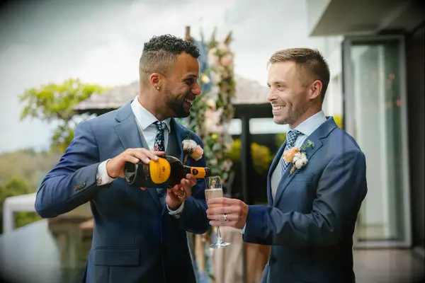 two grooms smile and pour champagne wearing navy blue suits