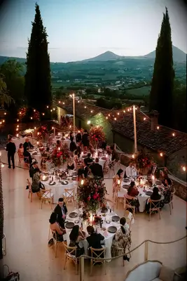 Lights twinkle dreamily overhead at a wedding reception, with views of the rolling Italian hills.