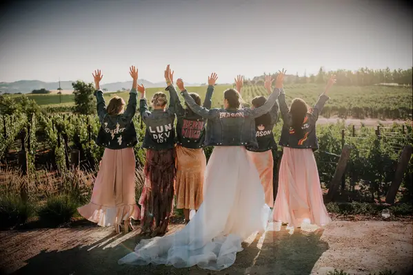 Bride and bridesmaid in vineyard posing in custom denim jackets