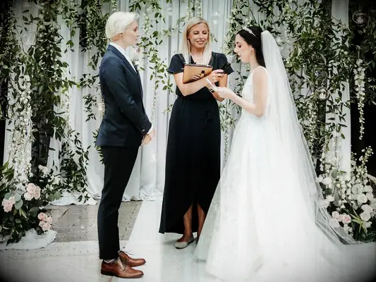 wedding officiant couple reading vows in front of flower wall