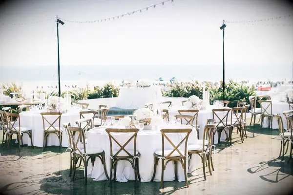 beach wedding reception with round tables and wooden cross back chairs beneath strands of bistro lights