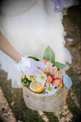 Flower girl wearing gloves holding a basket of daisies, flower buds, and lemon
