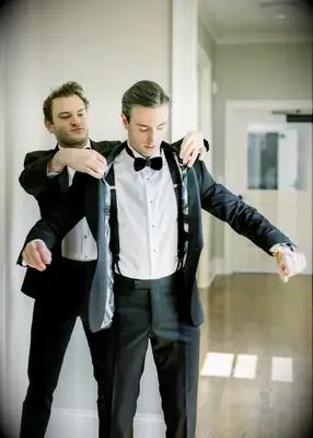 Best man helping groom try on tux