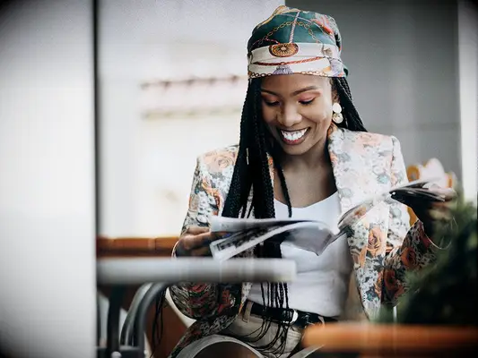 Woman in a floral blazer and matching headwrap reading a magazine.