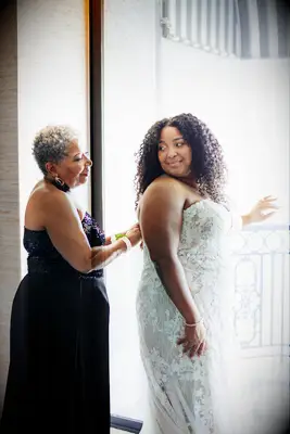 Mother of the bride helping daughter zip up wedding dress 