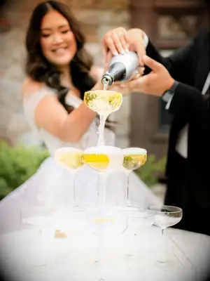 Bride and groom pour champagne for their Gatsby champagne tower. 