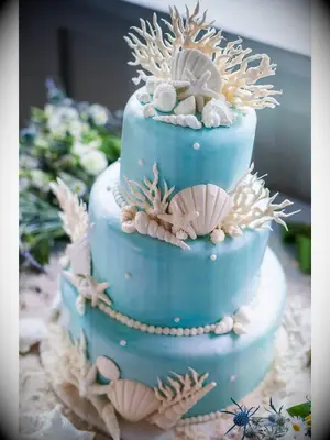 Three-tier blue beach wedding cake with white seashells and coral decor